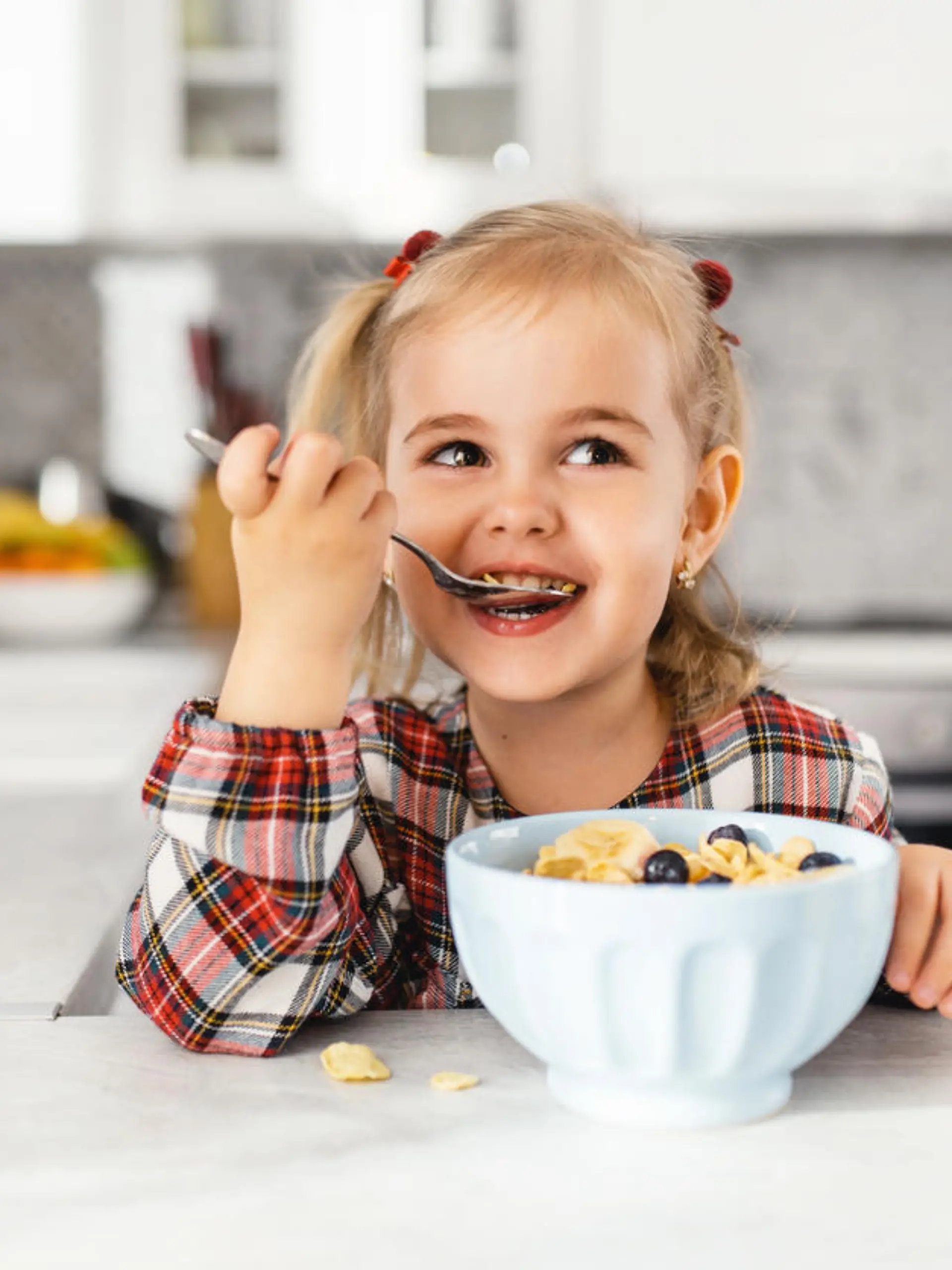 Beautiful little girl having breakfast with cereal, milk and blueberry in kitchen