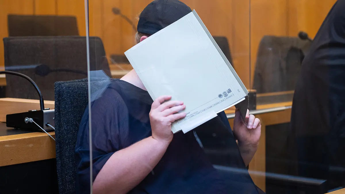 05.08.2021, Nordrhein-Westfalen, Münster: Zu Beginn des Prozesses im Missbrauchskomplex Münster sitzt die Mutter eines Opfers im Landgericht Münster und verdeckt ihr Gesicht mit einer Mappe. Die Anklage wirft der 31-Jährigen vor, den schweren sexuellen Missbrauch ihres heute elfjährigen Sohnes durch ihren Lebensgefährten nicht verhindert zu haben, obwohl sie davon wusste. Der IT-Techniker wurde im Hauptprozess zu 14 Jahren Haft und anschließender Sicherungsverwahrung verurteilt. Bis Ende September sind acht weitere Verhandlungstermine angesetzt. Foto: Guido Kirchner/dpa +++ dpa-Bildfunk +++