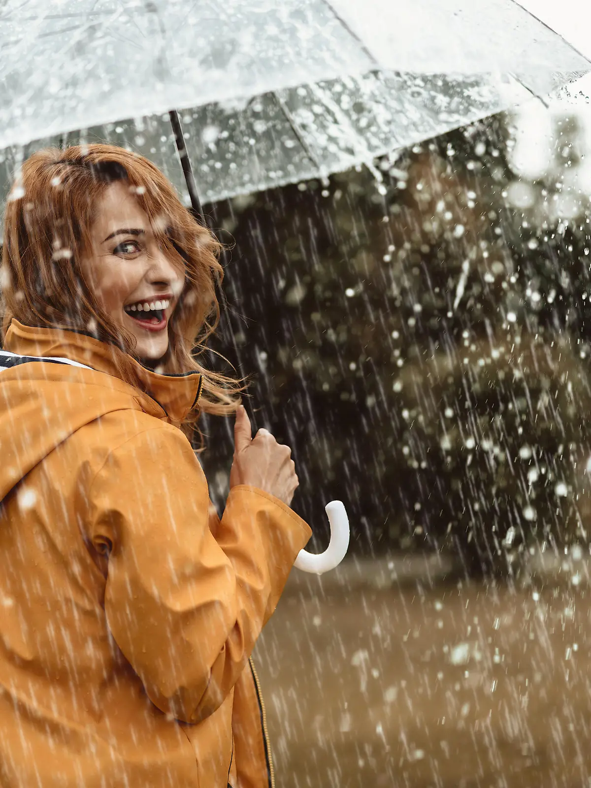 Cheerful pretty girl holding umbrella while strolling outside. She is turning back and looking at camera with true delight and sincere smile. Copy space in right side