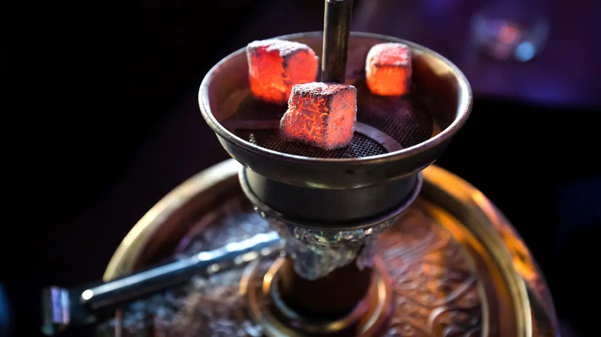 ARCHIV - 11.02.2019, Hamburg: Glühende Kohle liegt auf einem Metallsieb über dem Tabak im Kopf einer Wasserpfeife in einer Shisha-Bar. In NRW sind per Erlass neue strenge Regeln für Shisha-Bars in Kraft getreten. So müssen die Betreiber hochwirksame Lüftungsanlagen einbauen, Warnschilder am Eingang aufhängen und Warngeräte für Kohlenmonoxid (CO) in sämtlichen Gasträumen sowie im Thekenbereich, den Fluren und den Toiletten anbringen. Foto: Christian Charisius/dpa +++ dpa-Bildfunk +++