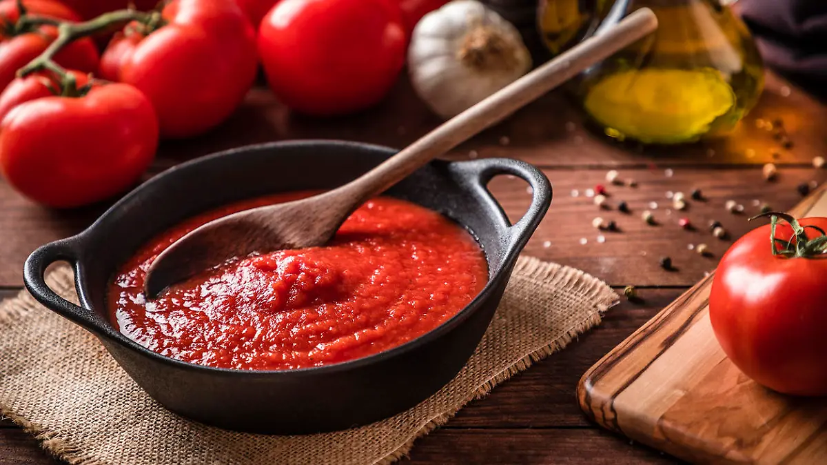 High angle view of a rustic cooking pan full of homemade tomato sauce surrounded by various tomatoes, garlic, pepper and olive oil for preparing the source. Predominant colors are brown and red, Studio shot taken with Canon EOS 6D Mark II and Canon EF 24-105 mm f/4L