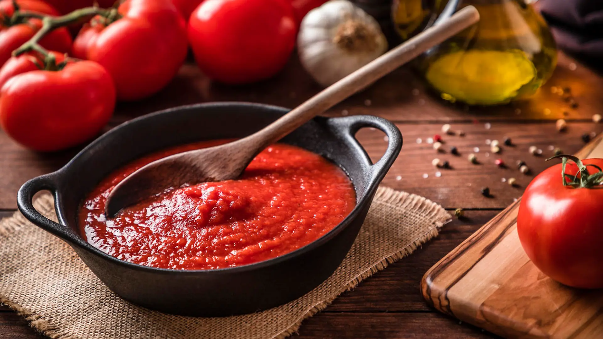High angle view of a rustic cooking pan full of homemade tomato sauce surrounded by various tomatoes, garlic, pepper and olive oil for preparing the source. Predominant colors are brown and red, Studio shot taken with Canon EOS 6D Mark II and Canon EF 24-105 mm f/4L