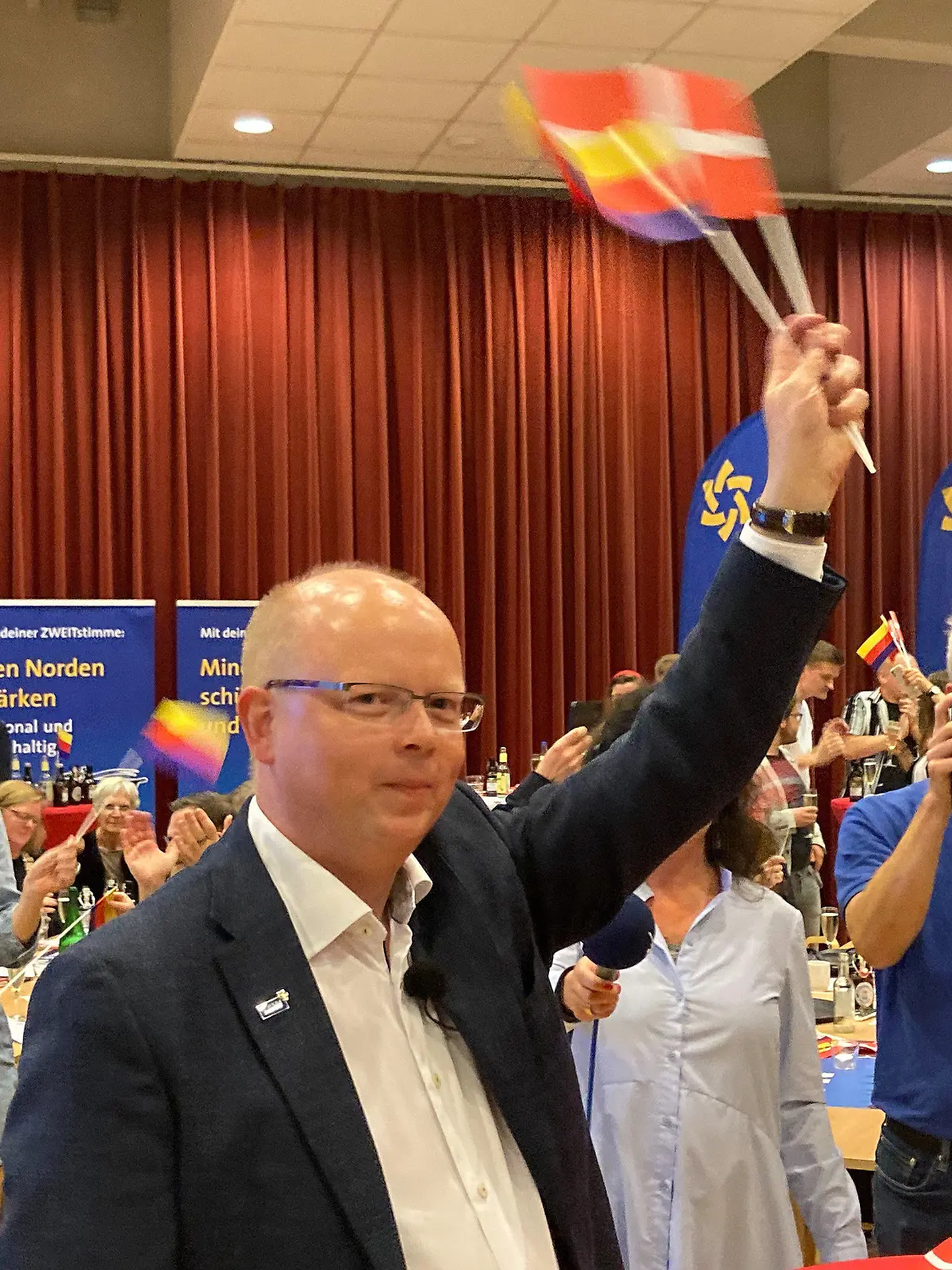 26.09.2021, Schleswig-Holstein, Flensburg: Stefan Seidler, Spitzenkandidat des Südschleswigschen Wählerverbandes (SSW) schwenkt auf der Wahlparty der Partei der dänischen Minderheit und der nationalen Friesen Fähnchen mit dem Dannebrog und den friesischen Farben. Die Partei ist bei der Bundestagswahl von der Fünf-Prozent-Hürde befreit. Foto: Birgitta von Gyldenfeldt/dpa +++ dpa-Bildfunk +++