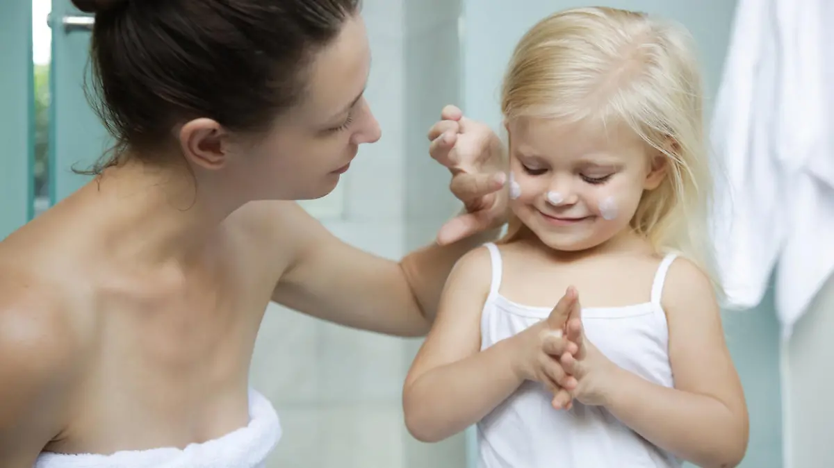 Mom applying cream on her daughter face in bathroom.