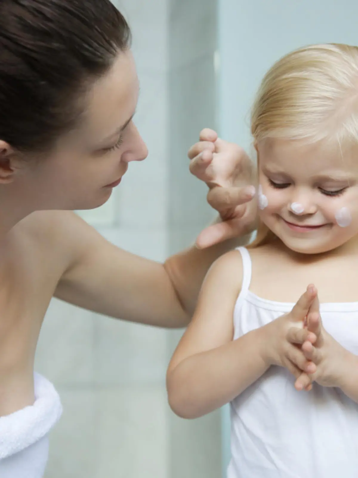 Mom applying cream on her daughter face in bathroom.