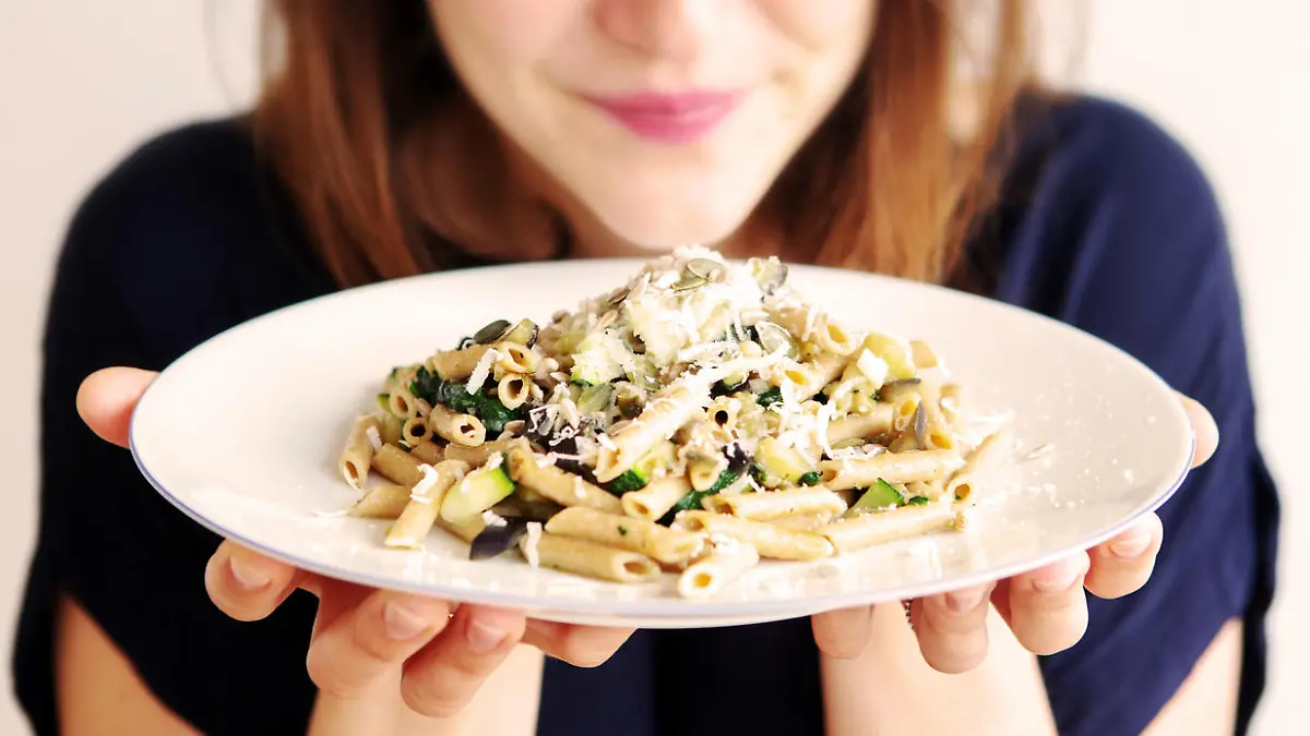 brunette young woman holding a white plate with pasta and cheese