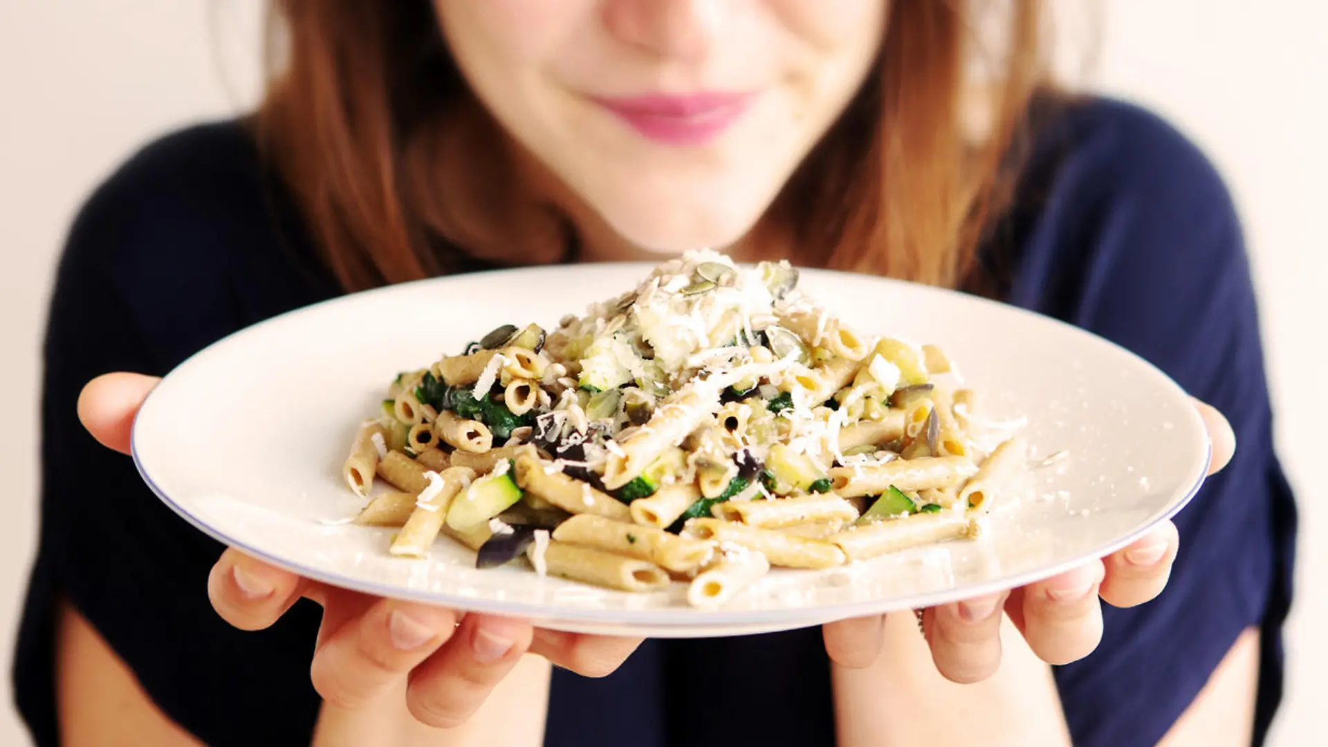 brunette young woman holding a white plate with pasta and cheese