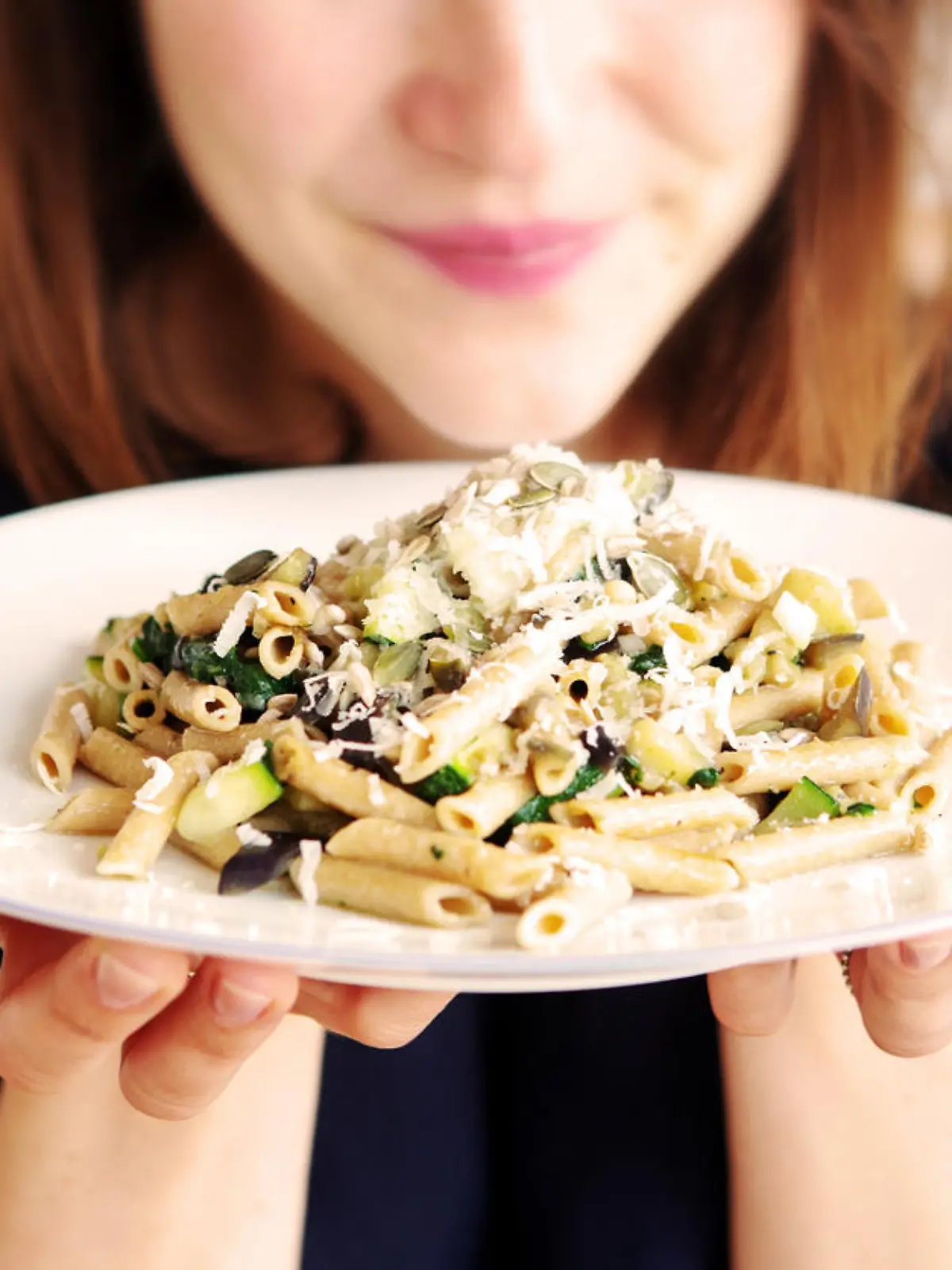 brunette young woman holding a white plate with pasta and cheese