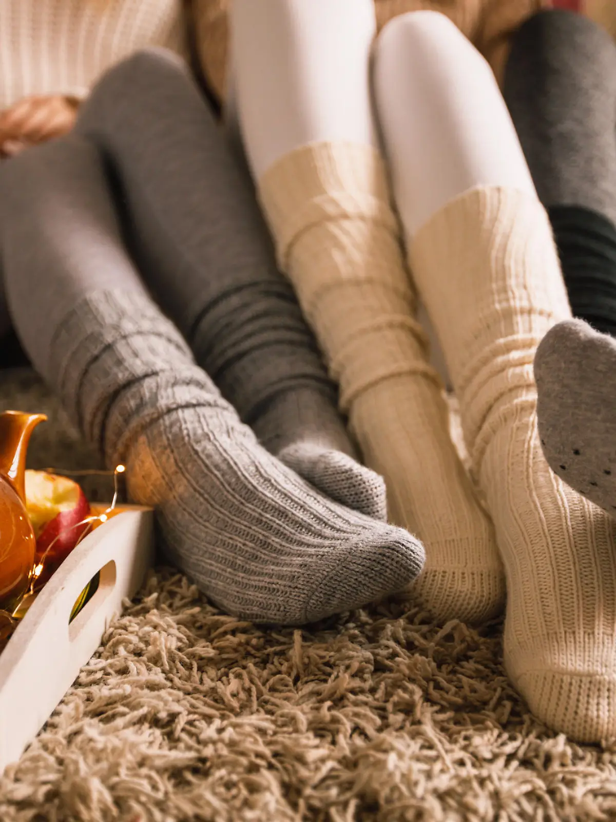 Lower section of three unrecognizable young girlfriends sitting on the bedroom floor in their cozy socks and hanging out together while enjoying some warm tea on a cold autumn day.