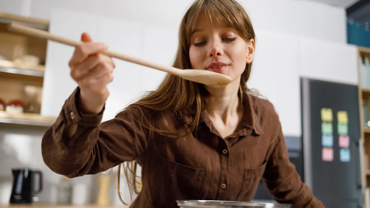 Pretty girl tasting food with wooden spoon while cooking