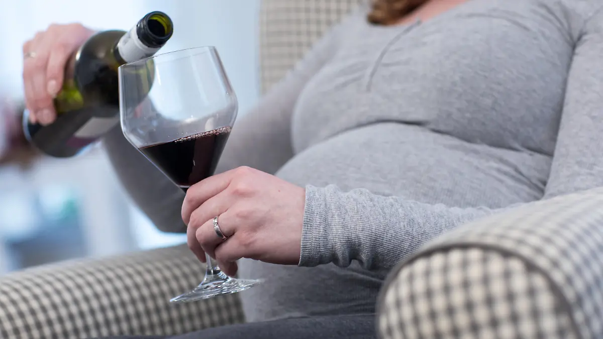 ILLUSTRATION - Eine schwangere Frau sitzt am 24.01.2018 in einer Wohnung in Bruchhausen-Vilsen (Niedersachsen) und giesst sich Rotwein in ein Glas (gestellte Szene). Foto: Christin Klose | Verwendung weltweit