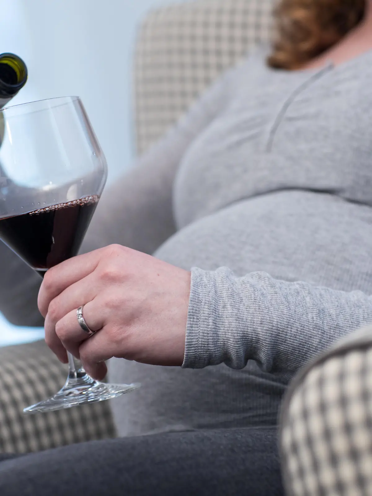 ILLUSTRATION - Eine schwangere Frau sitzt am 24.01.2018 in einer Wohnung in Bruchhausen-Vilsen (Niedersachsen) und giesst sich Rotwein in ein Glas (gestellte Szene). Foto: Christin Klose | Verwendung weltweit