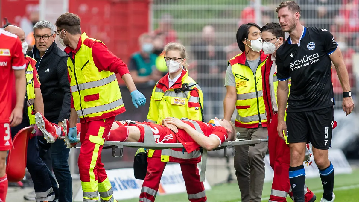 25.09.2021, Berlin: Fußball, Bundesliga, 6. Spieltag, 1. FC Union Berlin - Arminia Bielefeld, Stadion An der Alten Försterei: Berlins Timo Baumgartl wird nach einem Zusammenstoß mit Fabian Klos (r) von Arminia Bielefeld vom Spielfeld getragen. Links geht Berlins Trainer Urs Fischer. Foto: Andreas Gora/dpa - WICHTIGER HINWEIS: Gemäß den Vorgaben der DFL Deutsche Fußball Liga bzw. des DFB Deutscher Fußball-Bund ist es untersagt, in dem Stadion und/oder vom Spiel angefertigte Fotoaufnahmen in Form von Sequenzbildern und/oder videoähnlichen Fotostrecken zu verwerten bzw. verwerten zu lassen. +++ dpa-Bildfunk +++
