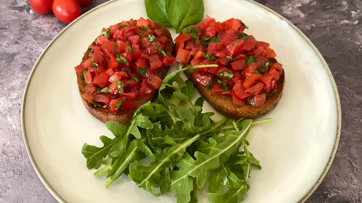 Italian bruschetta antipasto. Toasted white bread slices with garlic, olive oil, chopped cherry tomatoes, basil and arugula salad.