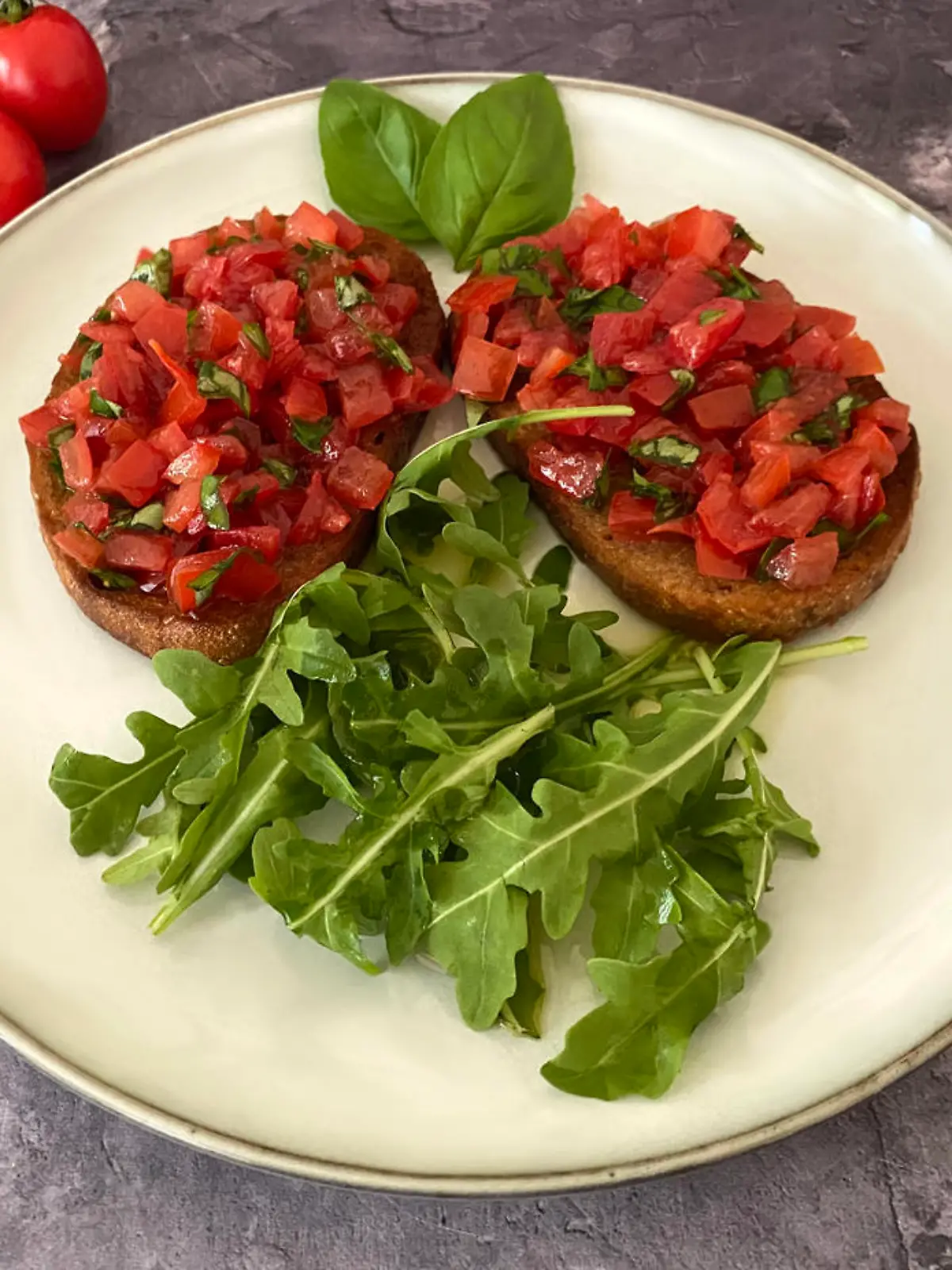 Italian bruschetta antipasto. Toasted white bread slices with garlic, olive oil, chopped cherry tomatoes, basil and arugula salad.