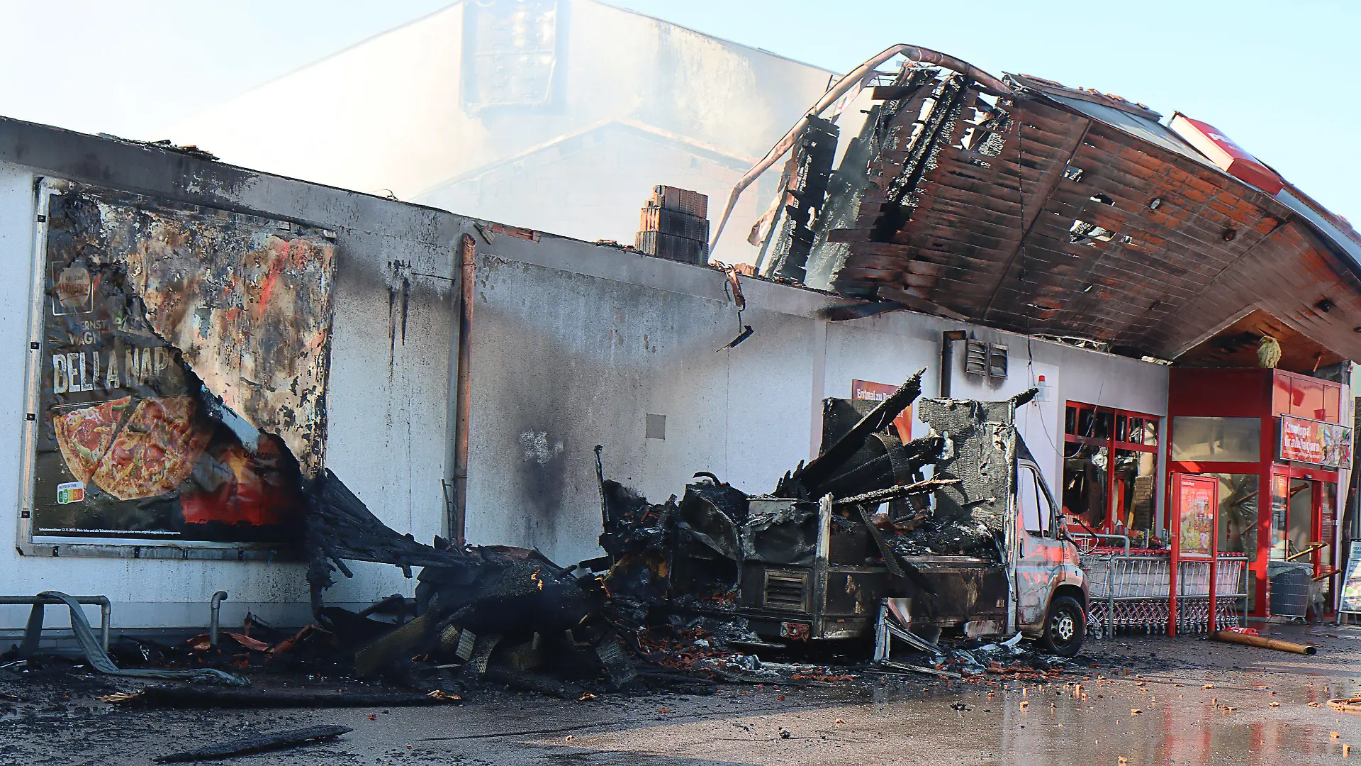 24.09.2021, Bayern, Allershausen: Nach einem Großbrand in einem Supermarkt sind Teile des Daches eingestürzt, ein verbrannter Kleinlaster steht an dem Supermarkt.  Das Feuer war am 24.09.2021 morgens in einem Penny-Markt ausgebrochen. Das Freisinger Landratsamt hatte die Bevölkerung aufgerufen, wegen der starken Rauchentwicklung Fenster und Türen geschlossen zu halten. Am späten Vormittag wurde die Warnung aufgehoben. Hinweise darauf, dass Menschen verletzt wurden, gab es demnach zunächst nicht. Foto: Mario Obeser/dpa +++ dpa-Bildfunk +++