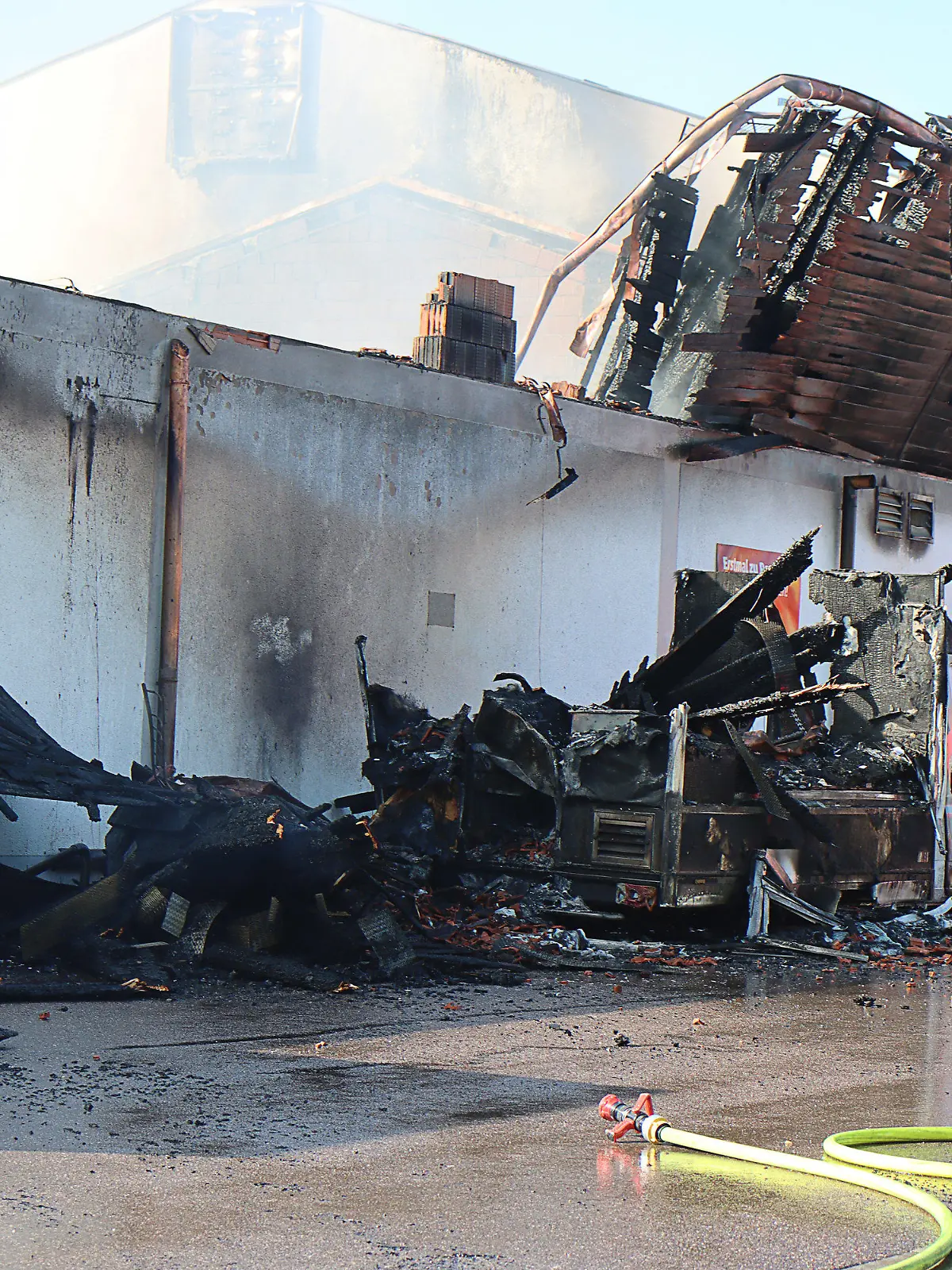 24.09.2021, Bayern, Allershausen: Nach einem Großbrand in einem Supermarkt sind Teile des Daches eingestürzt, ein verbrannter Kleinlaster steht an dem Supermarkt.  Das Feuer war am 24.09.2021 morgens in einem Penny-Markt ausgebrochen. Das Freisinger Landratsamt hatte die Bevölkerung aufgerufen, wegen der starken Rauchentwicklung Fenster und Türen geschlossen zu halten. Am späten Vormittag wurde die Warnung aufgehoben. Hinweise darauf, dass Menschen verletzt wurden, gab es demnach zunächst nicht. Foto: Mario Obeser/dpa +++ dpa-Bildfunk +++