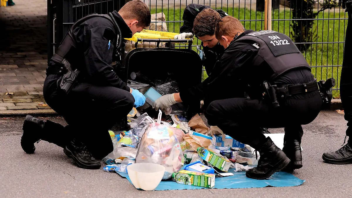 16.09.2021, Sachsen, Großröhrsdorf: Polizisten durchsuchen eine Mülltonne. Nachdem am Mittwochnachmittag eine 16-Jährige im Landkreis Bautzen getötet wurde, sucht die Polizei weiter nach dem Täter. Die Fahndung nach dem Mann läuft «auf Hochtouren», wie eine Sprecherin der Polizei mitteilte. Foto: Tino Plunert/dpa-Zentralbild/dpa +++ dpa-Bildfunk +++