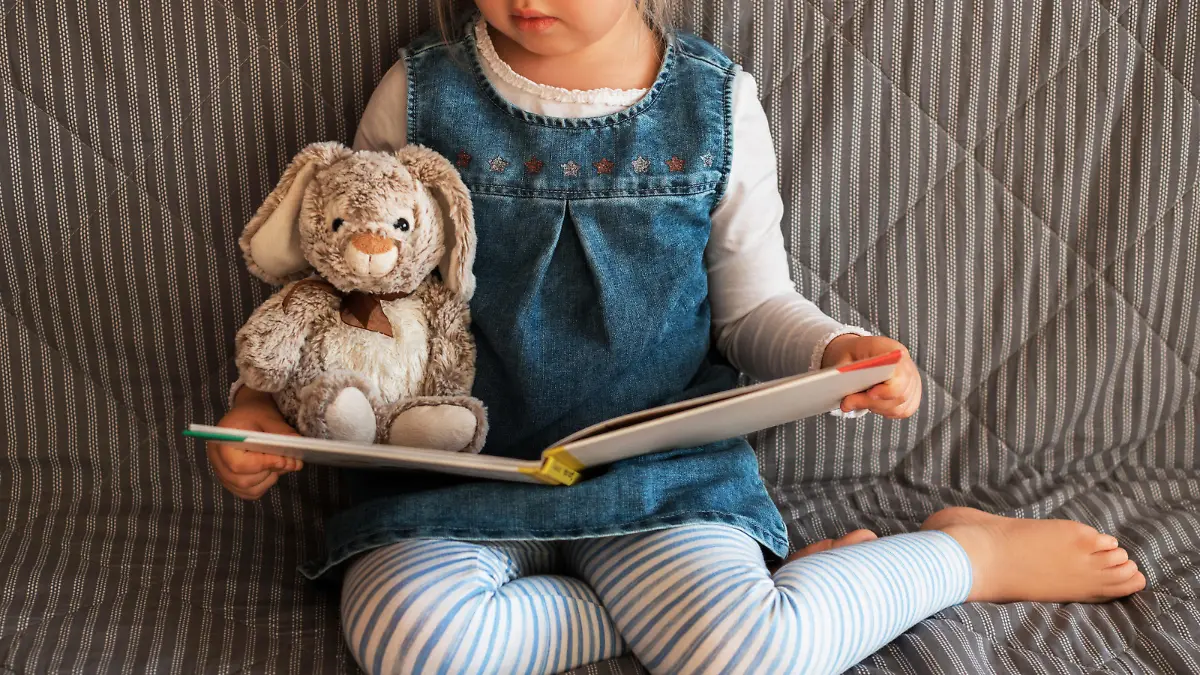 Little girl reading favorite book at home with her toy rabbit.