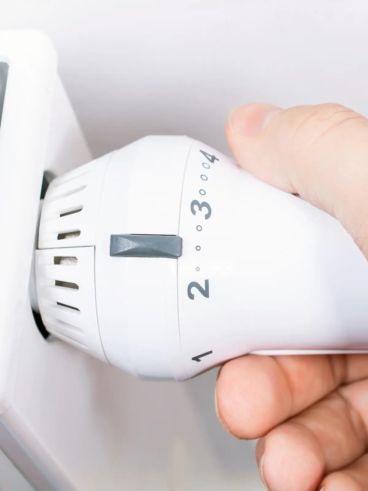 Male Hand Turns The Radiator Of A White Heater In The Living Room, Saving Energy Concept