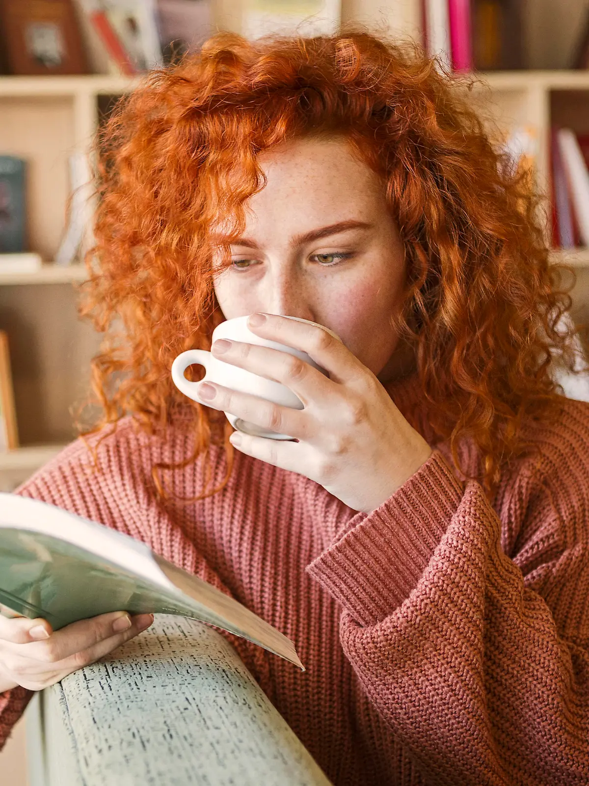 Woman sitting on sofa with mug of coffee reading a book