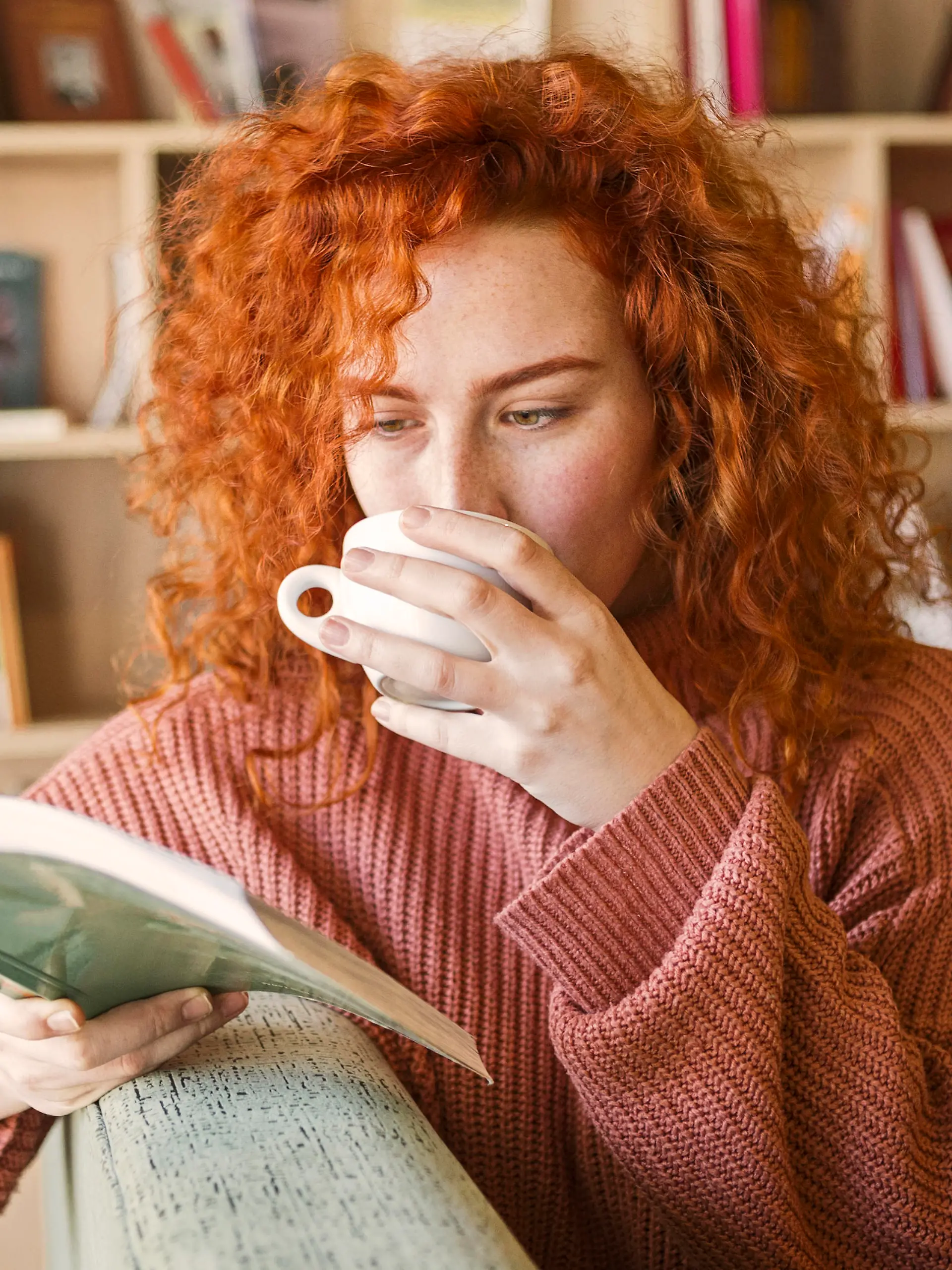 Woman sitting on sofa with mug of coffee reading a book