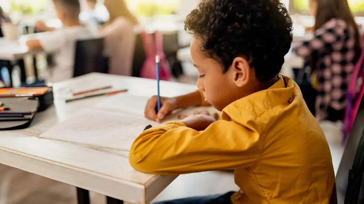 Black elementary student writing on the paper while having exam in the classroom.