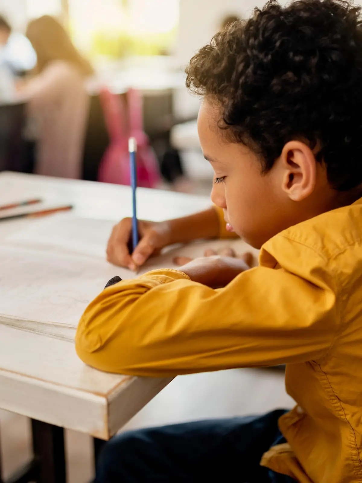 Black elementary student writing on the paper while having exam in the classroom.