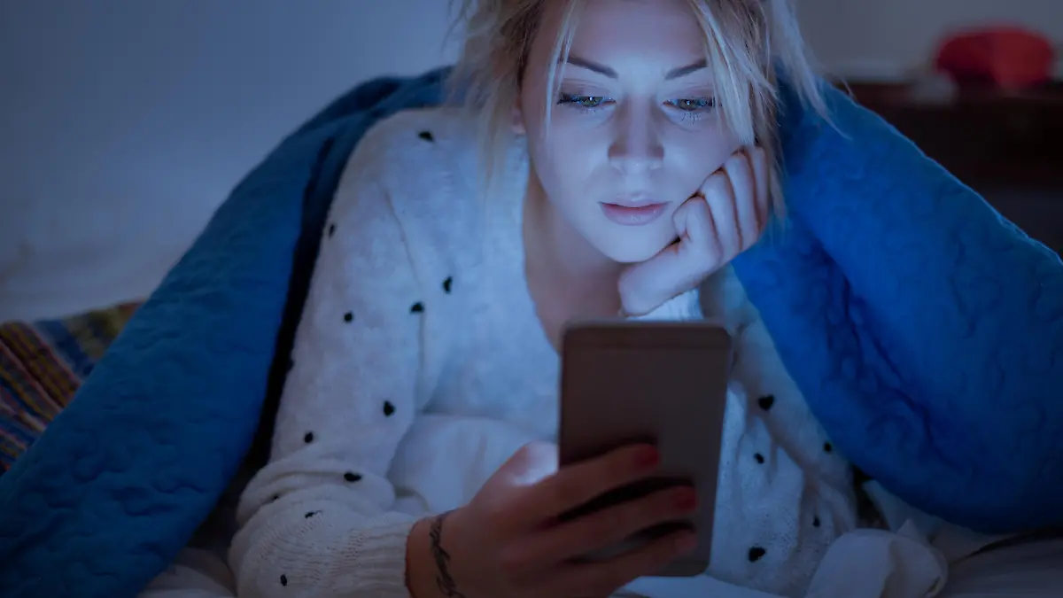 Disappointed sad woman holding mobile phone while laying on bed at night