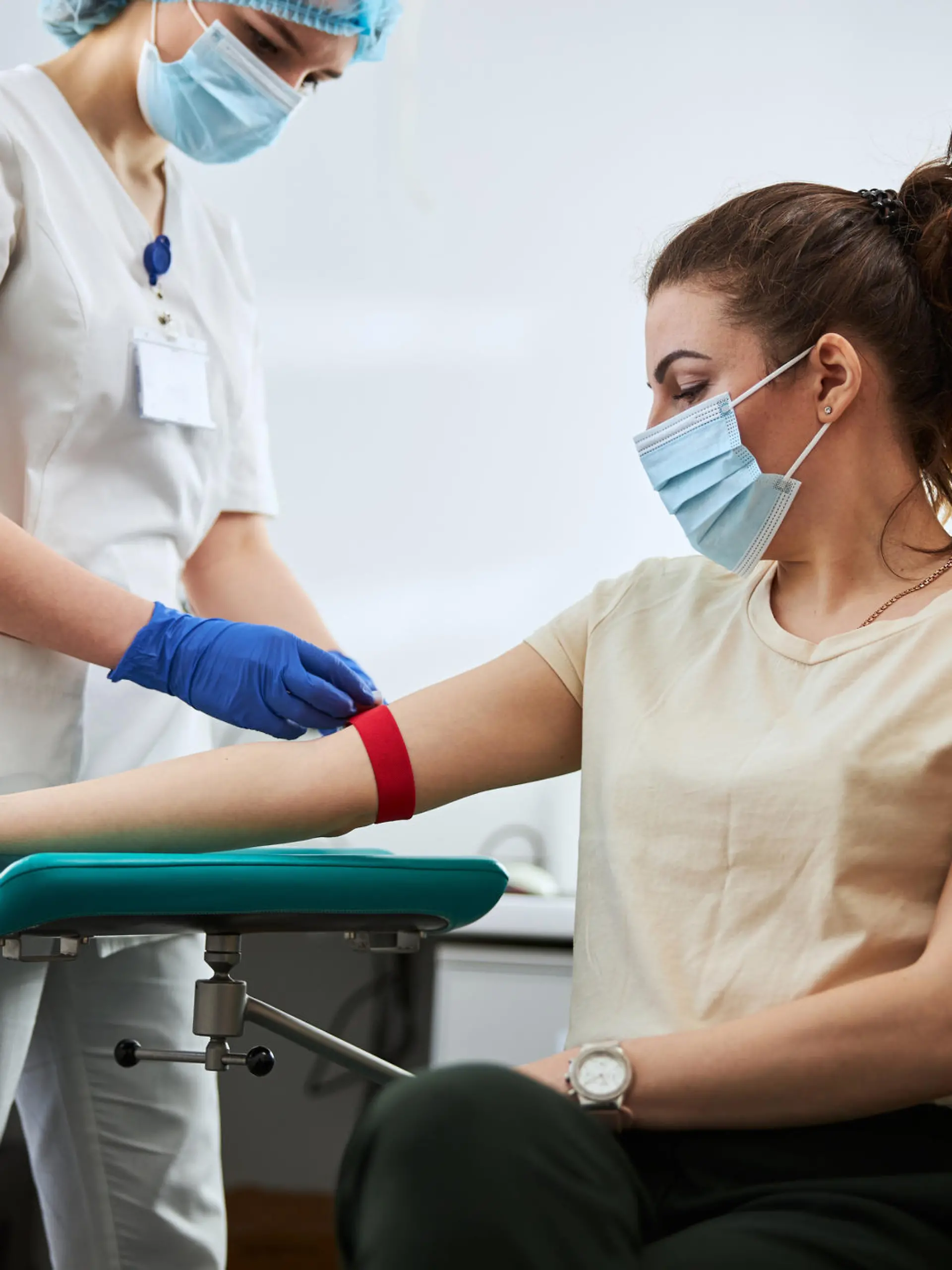 Skilled focused young phlebotomy technician applying a tourniquet to a female patient arm for venipuncture