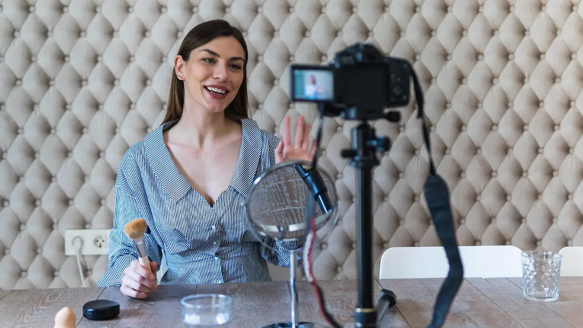 Cheerful attractive brunette in casual dress applying powder with brush on face while recording vlog video on camera, Model released, Property released Copyright: xPauxNovellx