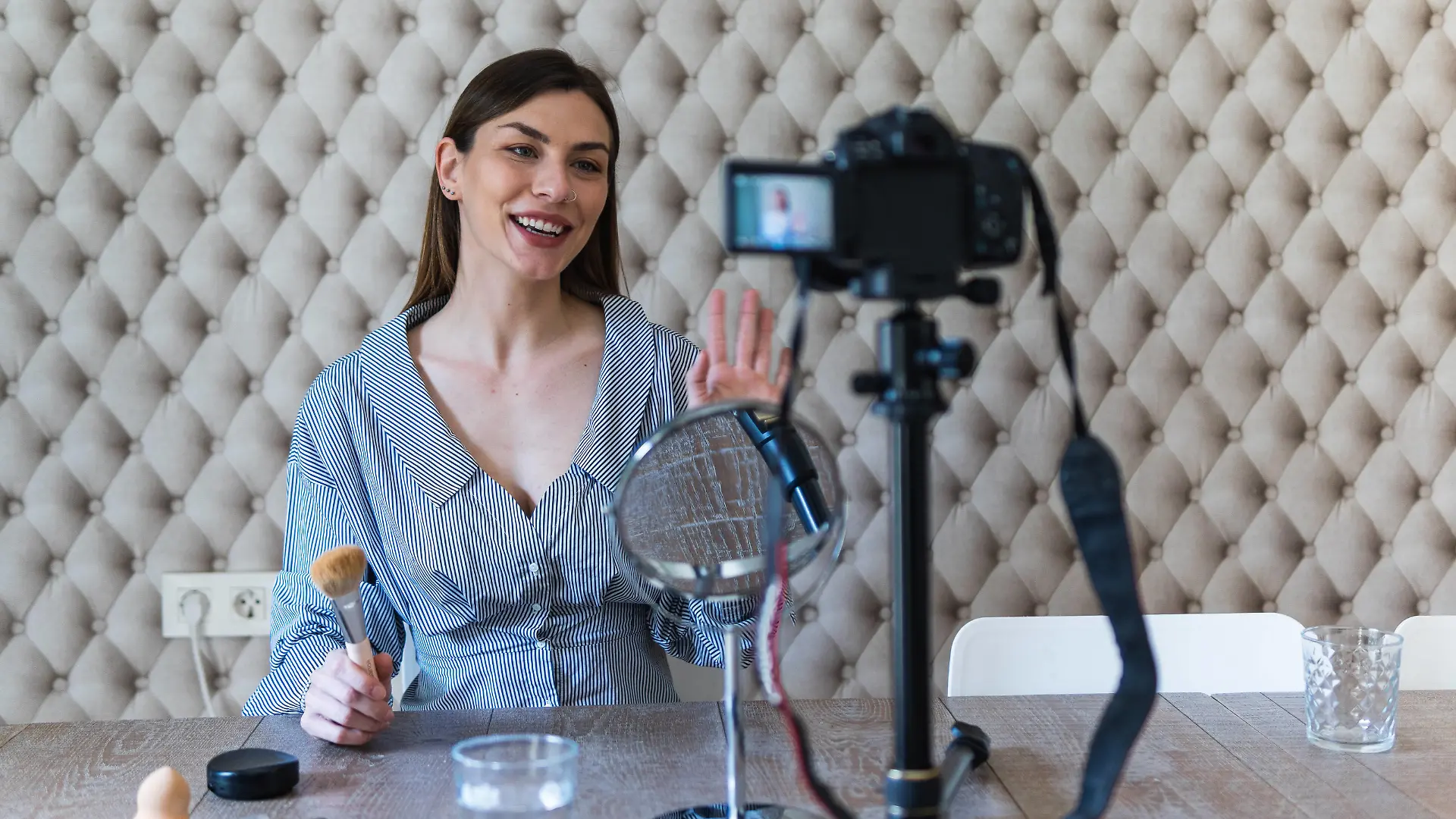 Cheerful attractive brunette in casual dress applying powder with brush on face while recording vlog video on camera, Model released, Property released Copyright: xPauxNovellx
