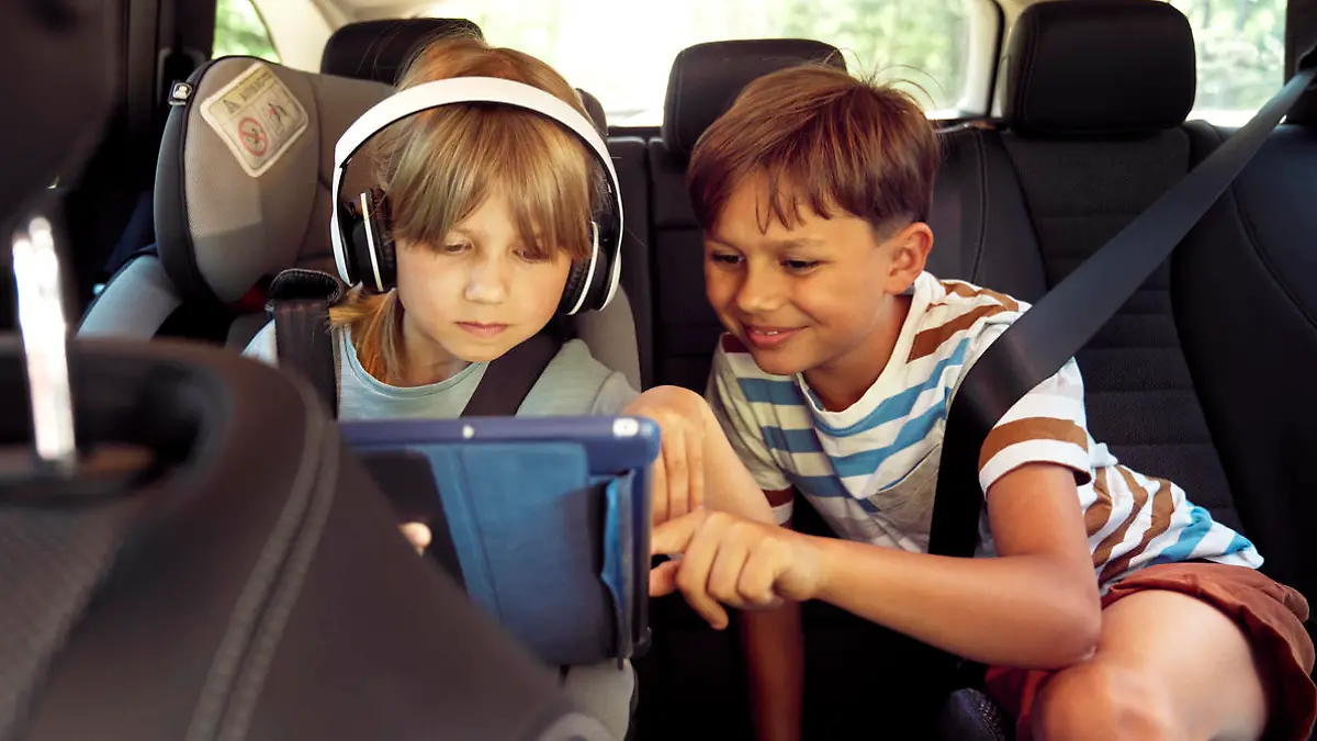                                 Happy siblings on rear seat of car with tablet