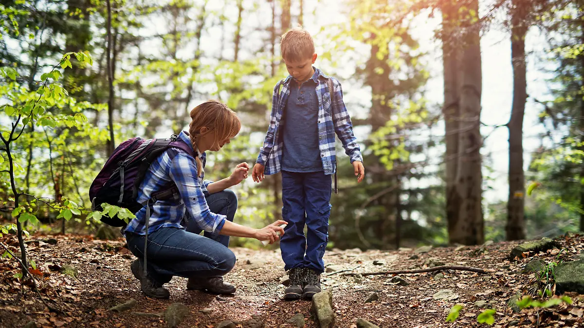 Mother and son hiking in forest. Mother is applying tick repellent on the son's legs.
Nikon D850