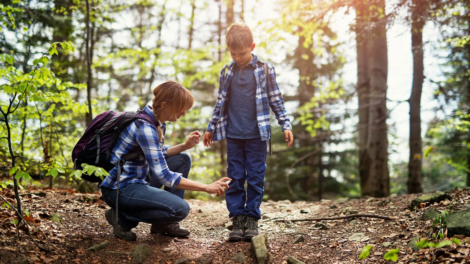 Mother and son hiking in forest. Mother is applying tick repellent on the son's legs.
Nikon D850