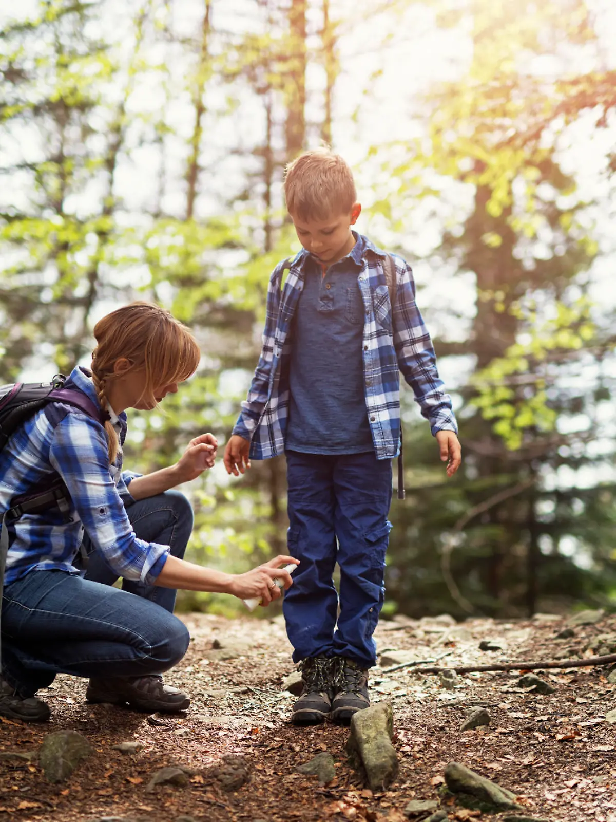Mother and son hiking in forest. Mother is applying tick repellent on the son's legs.
Nikon D850