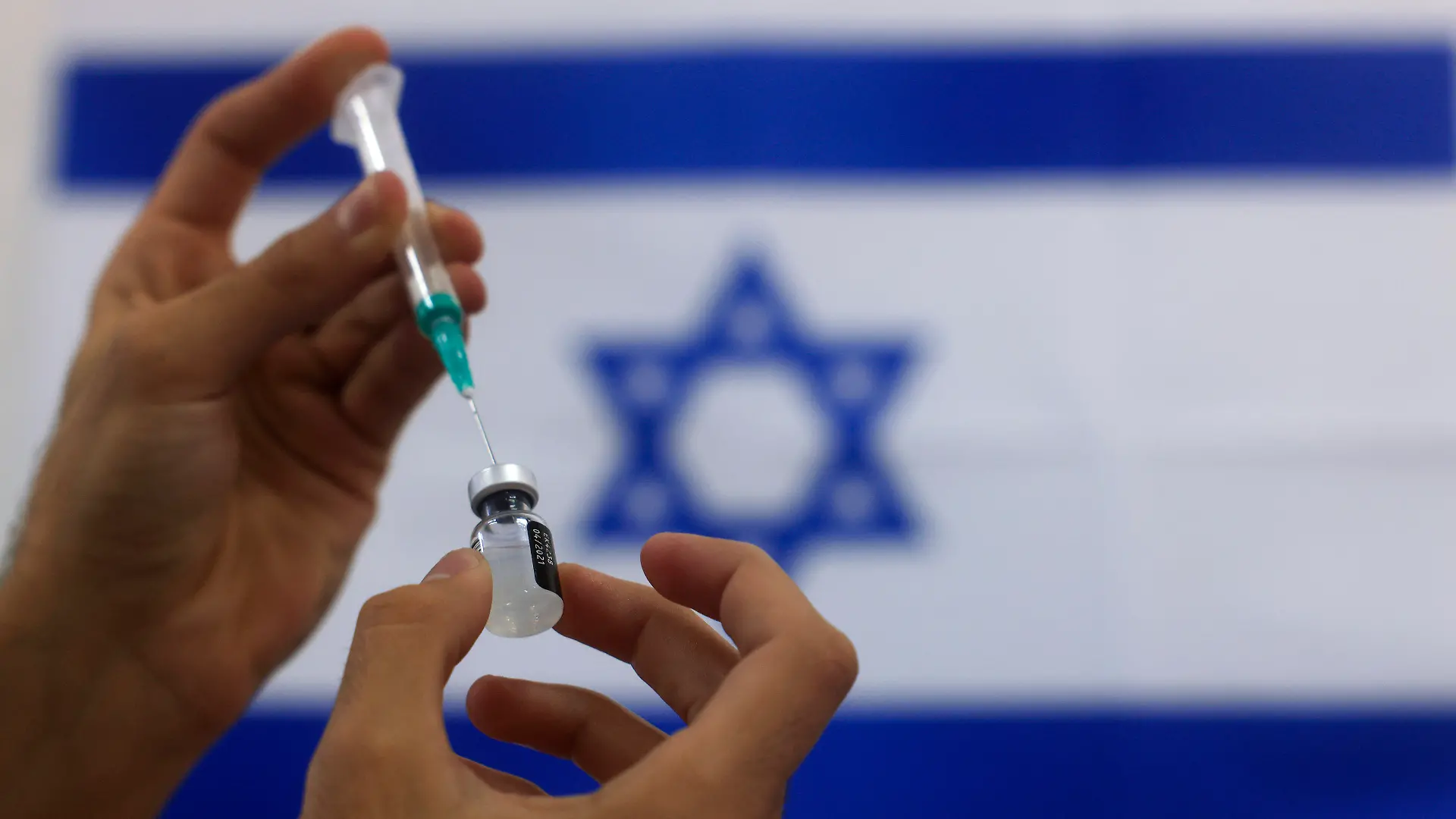 07.01.2021, Israel, Aschdod: Ein Sanitäter füllt vor der Flagge Israels den Corona-Impfstoff von Biontech/Pfizer in eine Spritze. In einer medizinischen Einrichtung in Aschdod sollen ältere Menschen gegen Corona geimpft werden. Foto: Tsafrir Abayov/AP/dpa +++ dpa-Bildfunk +++