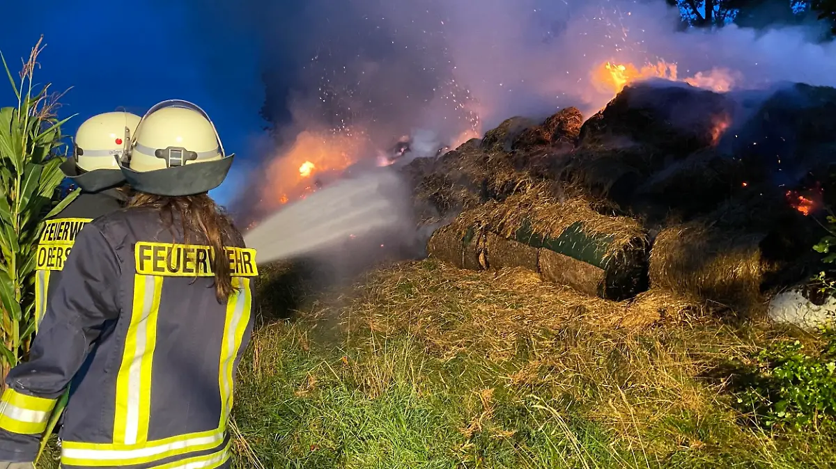 Feuerwehrmänner löschen die brennenden Heuballen.