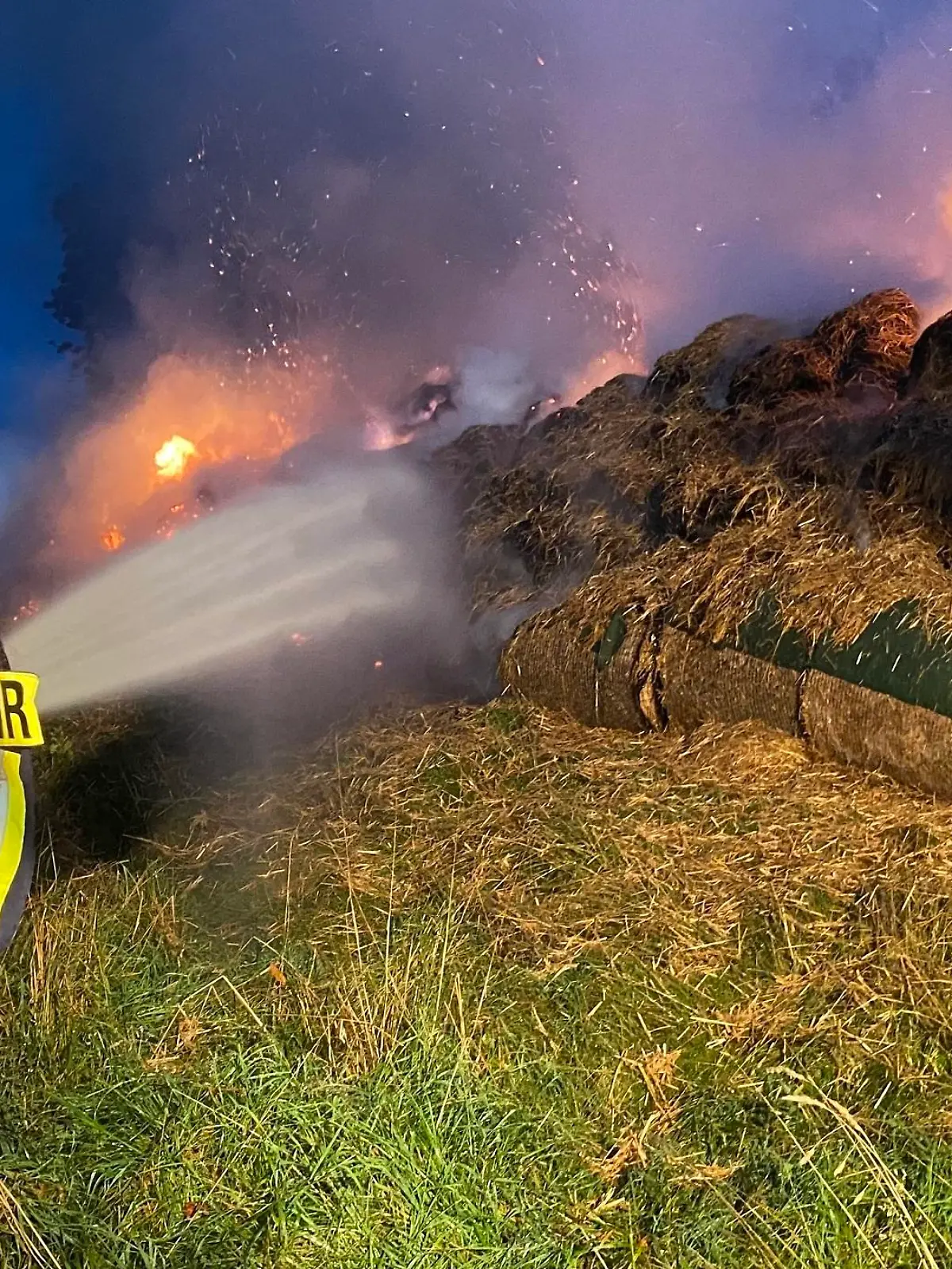 Feuerwehrmänner löschen die brennenden Heuballen.
