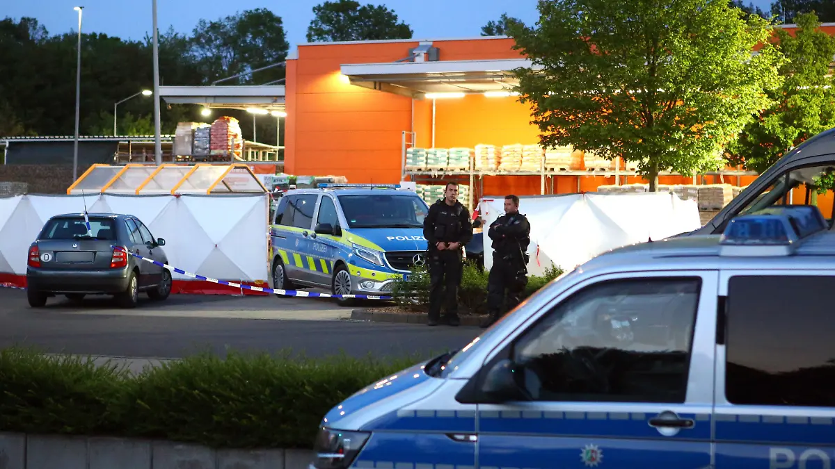 20.05.2023, Nordrhein-Westfalen, Aachen: Polizisten stehen am Tatort auf dem Parkplatz eines Baumarkts. In Aachen ist eine Frau am Samstagabend auf dem Parkplatz eines Baumarkts getötet worden. Die Polizei sperrte die Umgebung ab und setzte zur Fahndung einen Hubschrauber ein, wie ein Polizeisprecher am frühen Sonntagmorgen sagte. Schließlich wurde ein dringend Tatverdächtiger festgenommen. Die genauen Umstände und Hintergründe der Tat waren zunächst nicht bekannt. Eine Mordkommission übernahm die Ermittlungen zu dem Fall, über den zuvor die «Aachener Zeitung» berichtet hatte. Foto: Ralf Roeger/dpa - ACHTUNG: KfZ wurde aus rechtlichen Gründen gepixelt +++ dpa-Bildfunk +++
