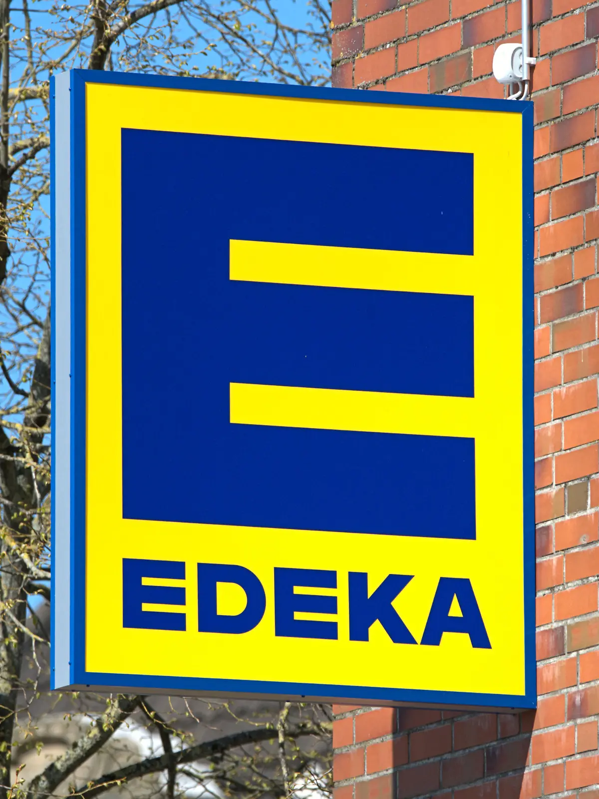 Schleswig, das Firmenschild eines Schleswiger EDEKA-Marktes an der roten Klinker-Fassade des Schlei-Centers. Die gelbe Leuchtreklame mit blauer Schrift der Handelskette bei schönem Frühlingswetter. Ein Großteil der Märkte der Edeka-Gruppe ist Inhabergeführt, die Edeka Zentrale Stiftung & Co. KG ist ein genossenschaftlich organisierter kooperativer Unternehmensverbund.
