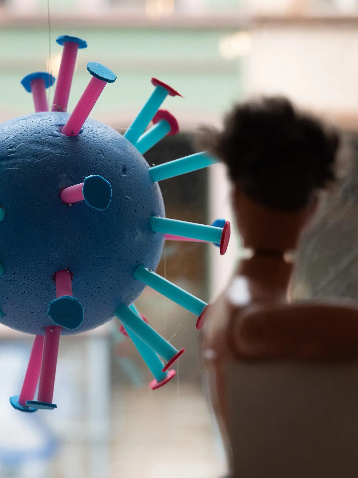 ARCHIV - 07.06.2021, Hessen, Frankfurt/Main: Ein stilisiertes Corona-Virus hängt in einem Schaufenster. Im Vordergrund ist eine Puppe zu sehen (zu dpa: «Inzidenz steigt kontinuierlich - Kommunen müssen Regeln verschärfen»). Foto: Sebastian Gollnow/dpa +++ dpa-Bildfunk +++