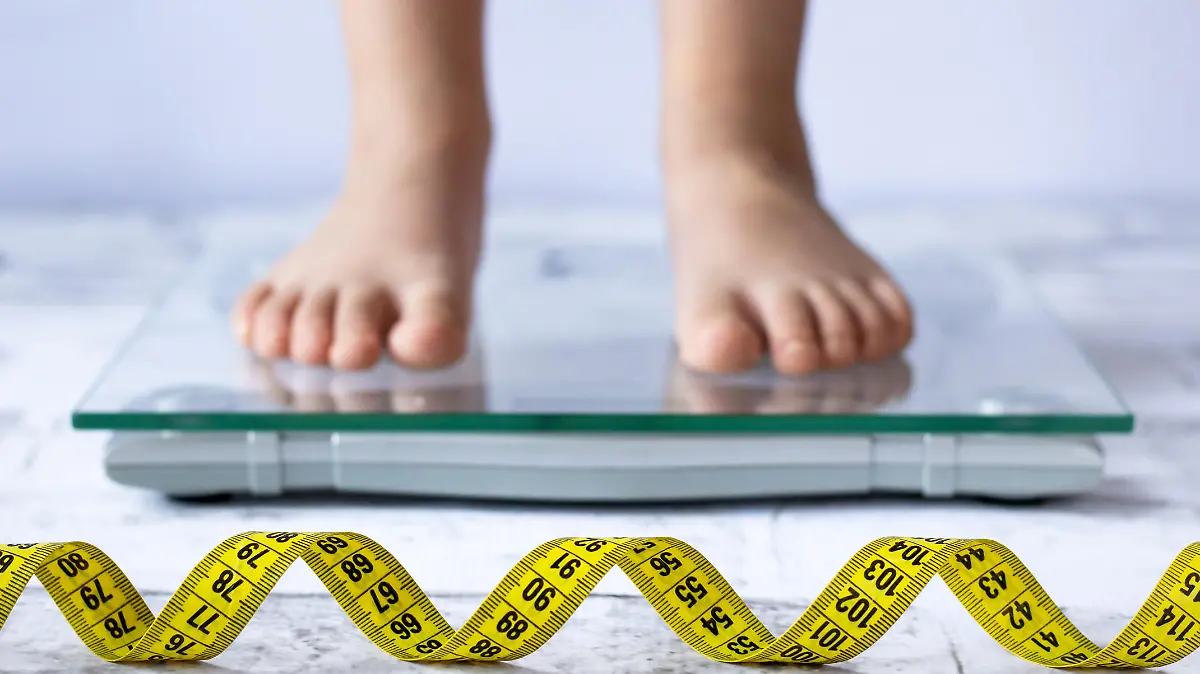 Weight control concept with centimeter in focus and blurred kid's feet on digital scale in the background. Child measuring weight, healthy growing.