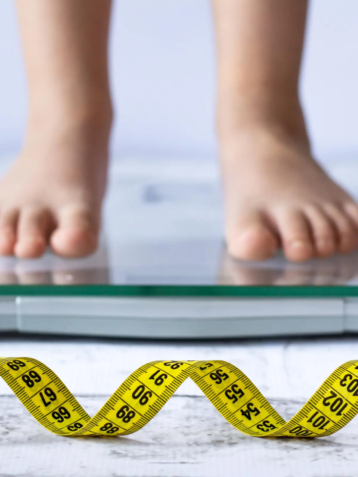 Weight control concept with centimeter in focus and blurred kid's feet on digital scale in the background. Child measuring weight, healthy growing.