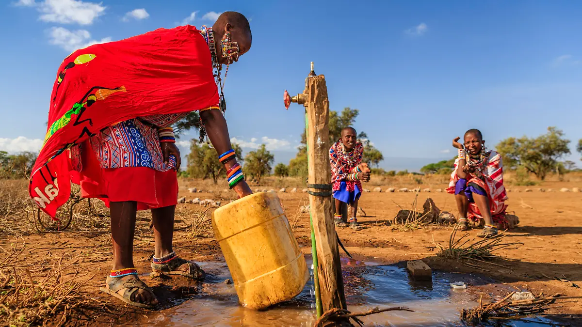 African woman from Maasai tribe collecting water to the tank, Kenya, Africa. When she finish filling the tank, she will carry water on her back to the village. African women and also children often walk long distances through the savanna to bring back containers of water. Some tourist camps cooperating with nearby villages and allow local people to use their water. Maasai tribe inhabiting southern Kenya and northern Tanzania, and they are related to the Samburu.