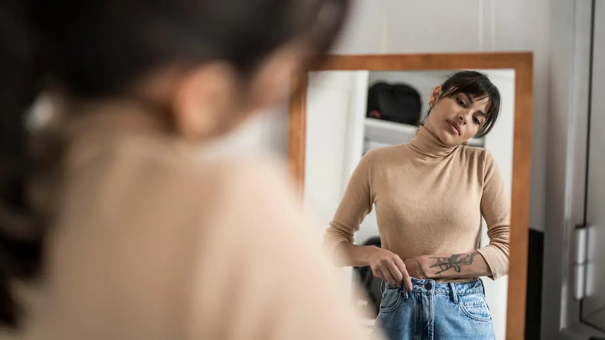 Young woman getting dressed in front of a mirror at home