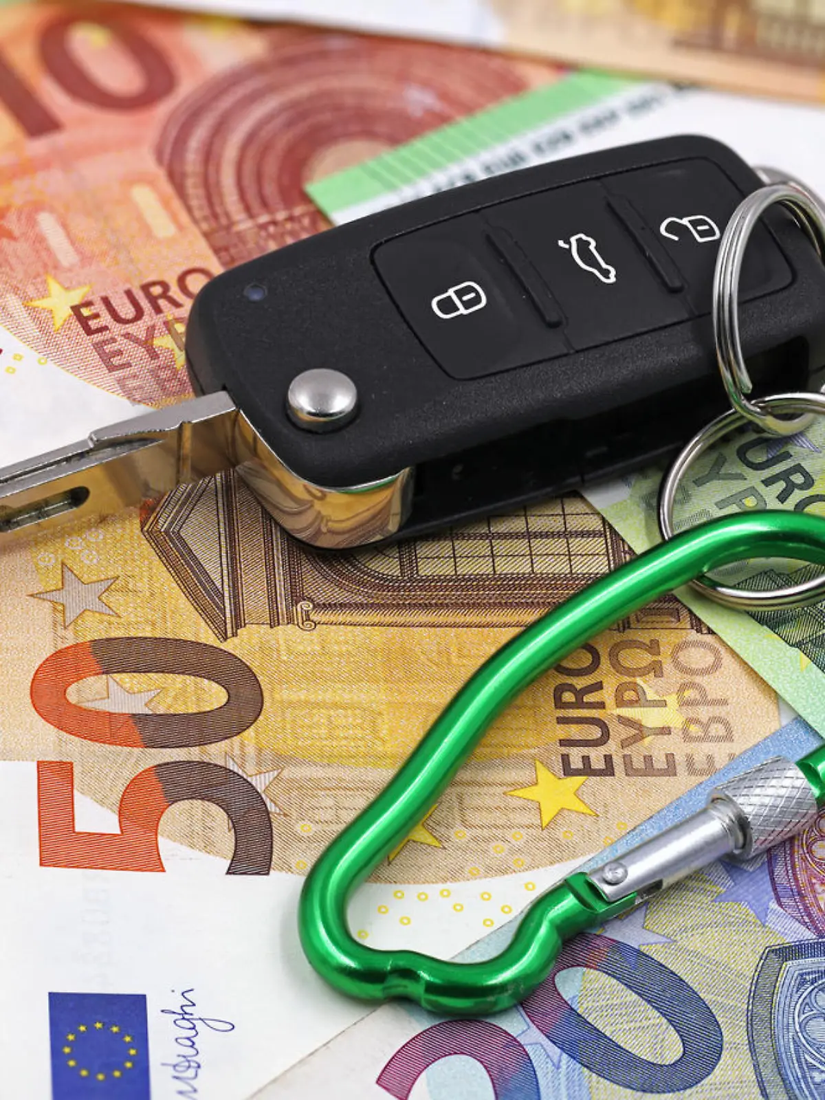 car key with carabiner in car shape on euro money background, concept of car insurance.