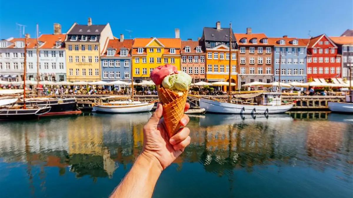 Mensch hält Eiswaffel in die Kamera vor den bunten Häusern am Nyhavn in Kopenhagen.