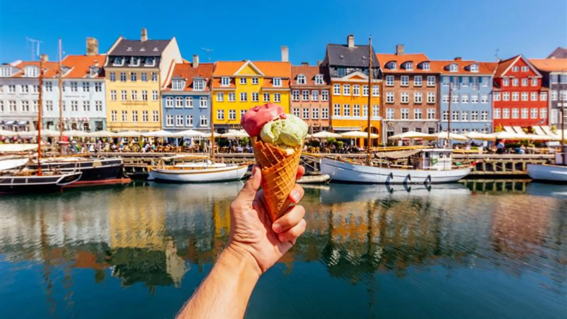 Mensch hält Eiswaffel in die Kamera vor den bunten Häusern am Nyhavn in Kopenhagen.