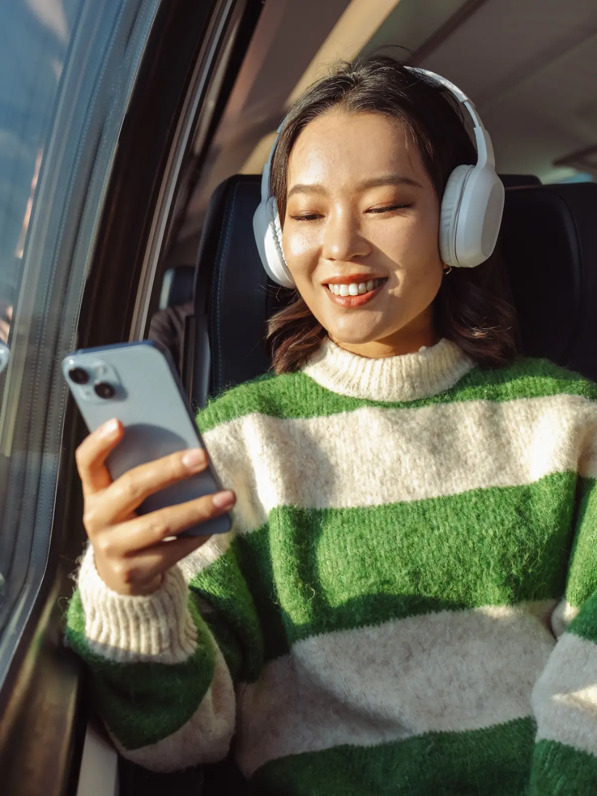 Eine junge asiatische Frau sitzt im Zug und schaut auf ihr Handy. Sie ist glücklich.